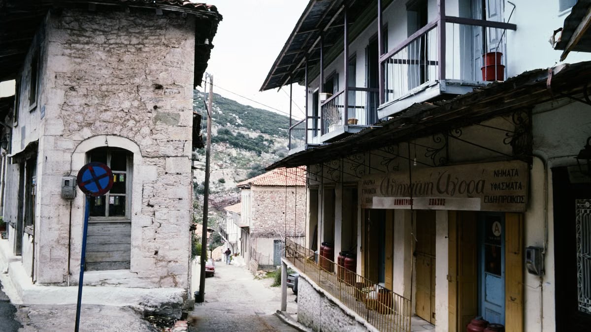 Picturesque street scene in a quaint Greek village featuring rustic stone houses and scenic mountain backdrop.